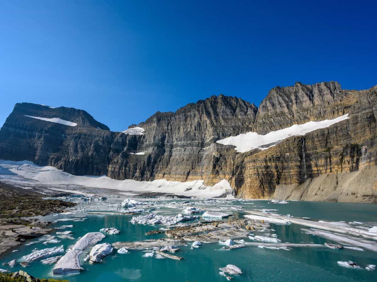 Stunning view of Grinnell Glacier in Glacier National Park, with floating icebergs on turquoise glacial water beneath towering rock walls and streaks of snow—one of the best hikes in Glacier National Park for dramatic alpine scenery.