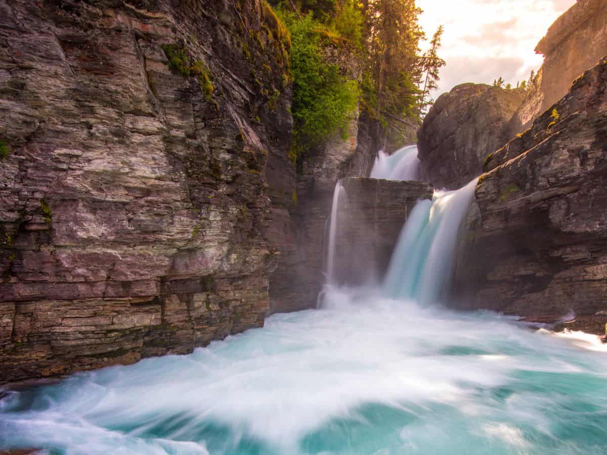 Rushing turquoise water cascades down St Marys Falls in Glacier National Park, framed by rugged rock walls and glowing sunset light—one of the best hikes in Glacier National Park for waterfall lovers.