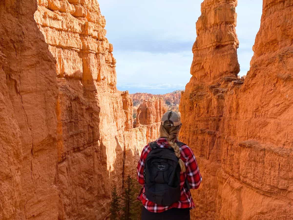 Woman with a backpack looking out between towering orange rock walls along a Bryce Canyon trail, capturing the awe-inspiring views typical of one day in Bryce Canyon National Park.