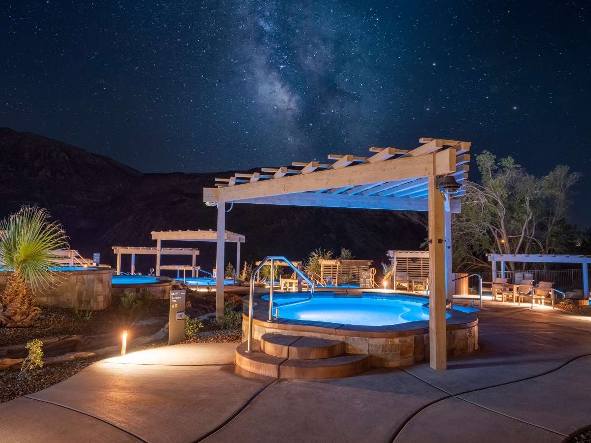 Outdoor hot tubs glow under a star filled night sky with the Milky Way visible above a desert landscape near Zion National Park. This relaxing spa setting offers a unique way to unwind and stargaze as part of a Zion National Park itinerary after a day of hiking.