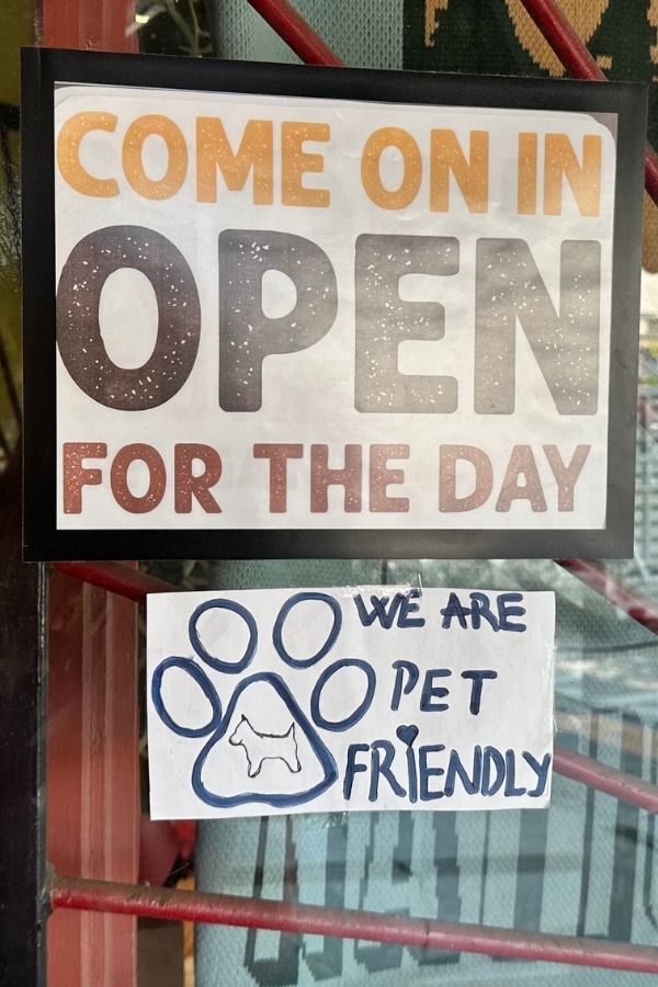 are dogs allowed in Acadia National Park? A shop window displays two signs, one reading “Come on in, open for the day” and another with a paw print illustration that says “We are pet friendly.” This complements “Are dogs allowed in Acadia National Park” by showing local businesses that welcome pets alongside park visitors.