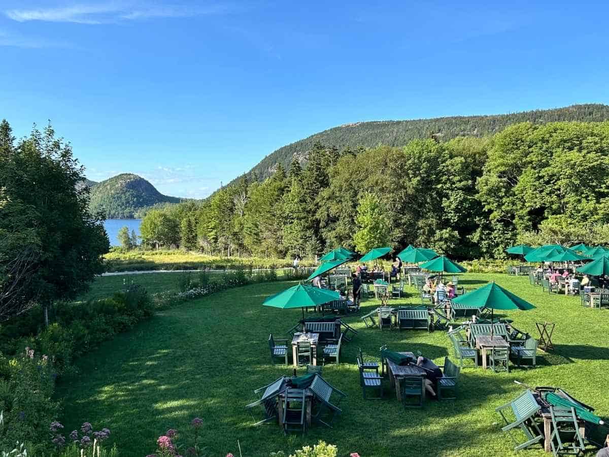 are dogs allowed in Acadia National Park? Outdoor seating with green umbrellas is set on a grassy lawn at Jordan Pond House overlooking the lake and forested mountains in Acadia National Park. While no pets are pictured, the scene connects to “Are dogs allowed in Acadia National Park” by showing one of the relaxing, dog-friendly areas where visitors can unwind.