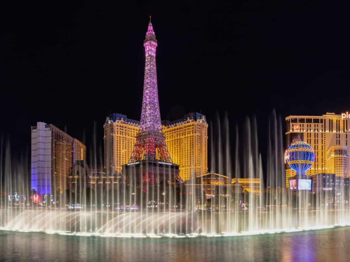 Night view of the Las Vegas Strip featuring the illuminated Eiffel Tower replica at Paris Las Vegas and the Bellagio fountain show in full spray. A vibrant kickoff location for a Las Vegas to Grand Canyon road trip.