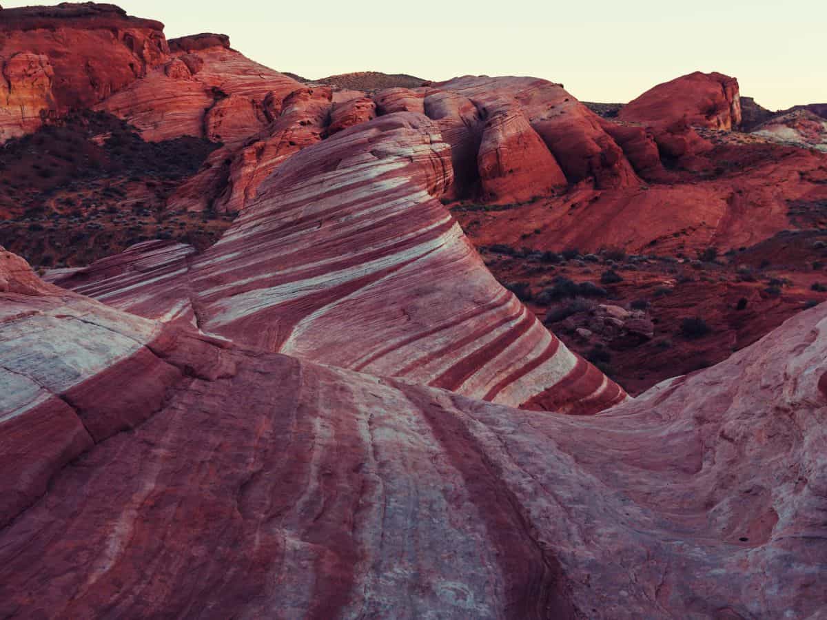 Wave like red and white striped sandstone formation surrounded by glowing desert cliffs at sunset, a striking stop on a las vegas to zion national park road trip. The swirling rock patterns and warm evening light showcase the unique geological landscapes travelers can explore between Las Vegas and Zion.