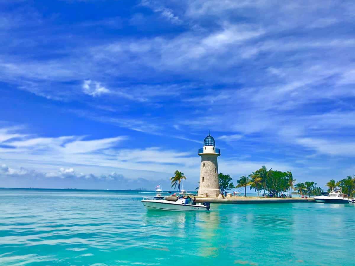A white lighthouse stands on a palm-lined shore surrounded by turquoise waters and boats at Biscayne National Park. Known for boating, snorkeling, and warm coastal weather, it’s one of the best national parks to visit in November for tropical vibes without the crowds.