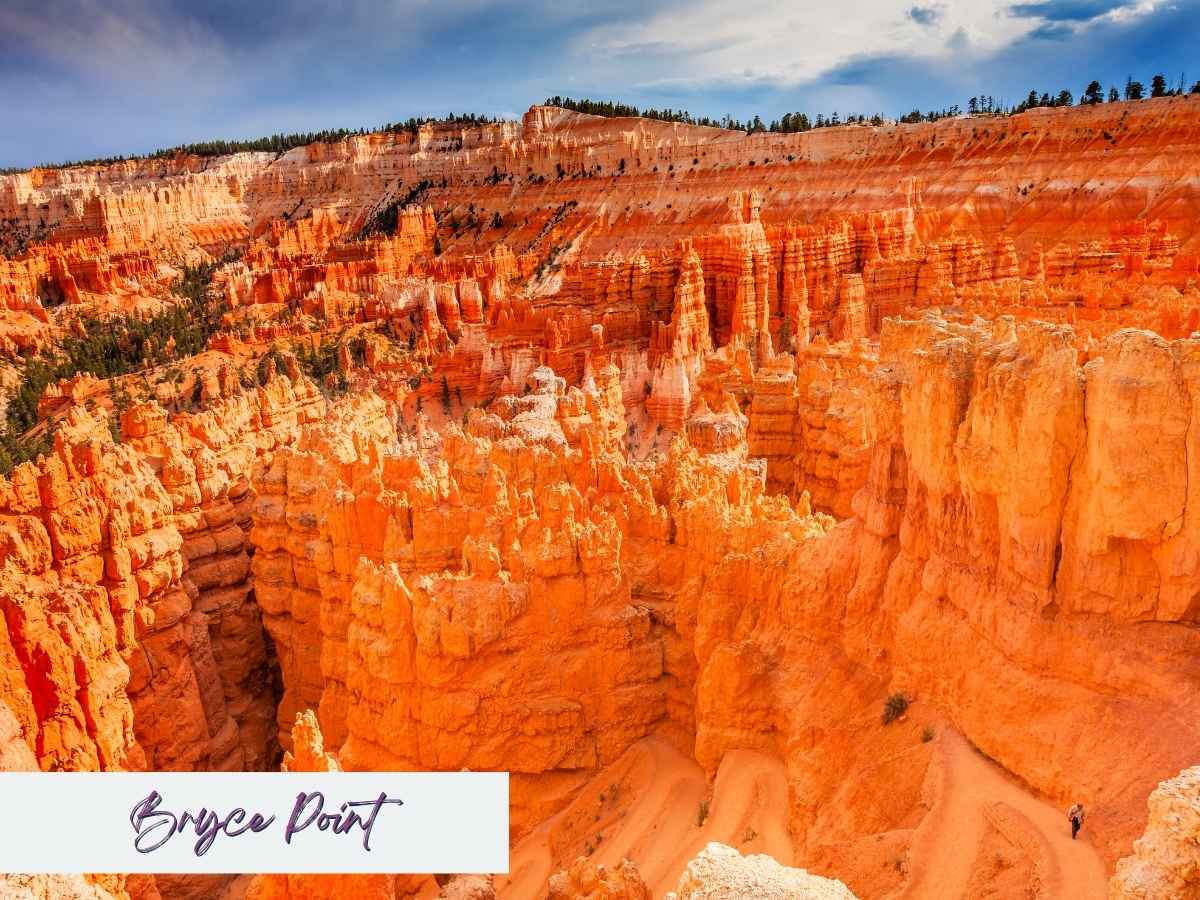 Panoramic view of Bryce Point in Bryce Canyon National Park, featuring a maze of vibrant orange hoodoos and winding switchback trails carved into the canyon floor. A lone hiker is visible on the lower right, highlighting the scale and dramatic beauty of one of the best Bryce Canyon hikes. Text overlay in the bottom left reads “Bryce Point” in a handwritten-style font.