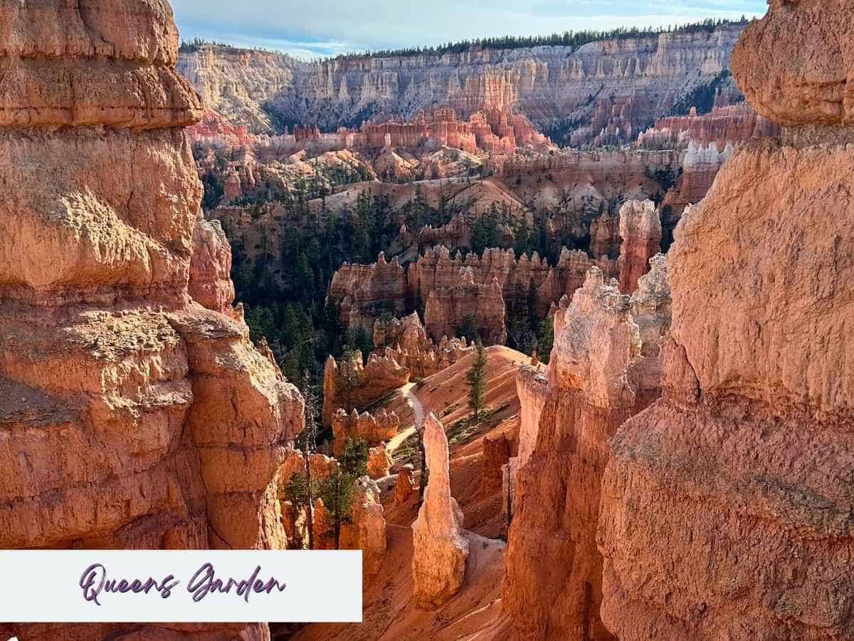 The Queens Garden Trail in Bryce Canyon National Park winds through towering orange and pink hoodoos, with layered cliffs and forested areas stretching into the background. Framed by massive rock formations, this scenic path offers one of the most accessible and breathtaking Bryce Canyon hikes. Text overlay in the bottom left reads “Queens Garden” in a script-style font.