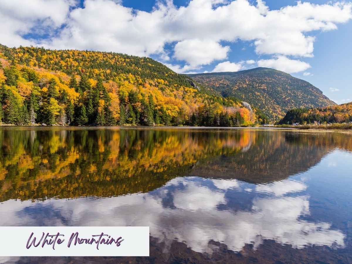 Bright autumn foliage and towering peaks reflected in a calm lake in New Hampshire’s White Mountains, a breathtaking nature destination on a 7 day New England road trip itinerary.