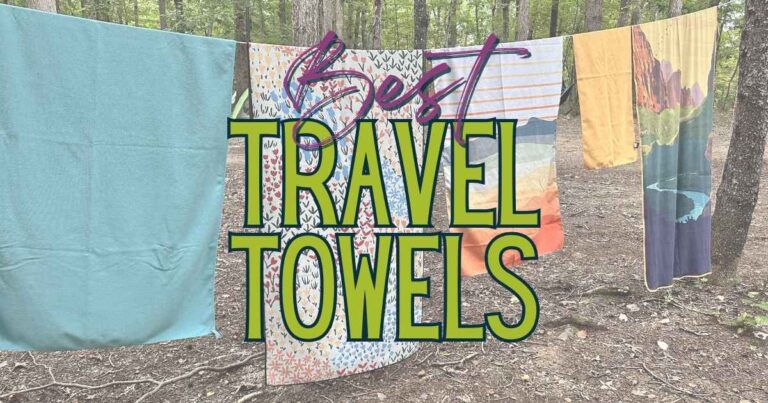Colorful travel towels hanging on a clothesline in a wooded campsite with the words Best Travel Towels overlaid across the center. The quick dry towels feature solid and scenic prints and are displayed outdoors to compare size and design for choosing the best travel towel for camping, backpacking, hiking or trips.