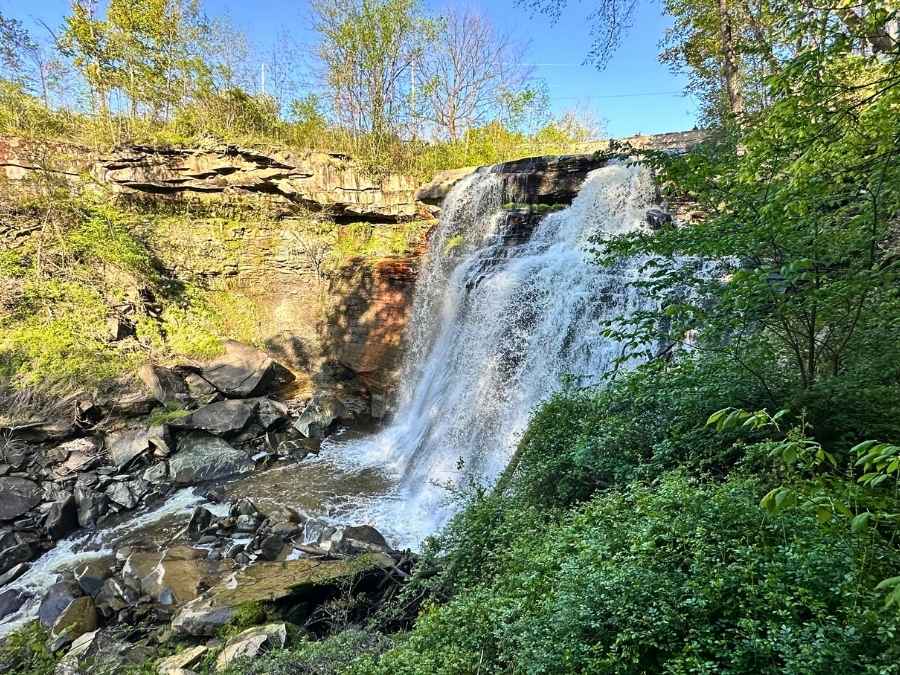 Brandywine Falls cascades powerfully over a rocky cliff surrounded by lush greenery in Cuyahoga Valley National Park. Visiting this iconic waterfall is one of the best things to do in Cuyahoga Valley National Park itinerary.